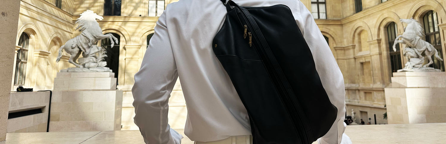 Person wearing a designer bag in front of classical sculptures at the Louvre architecture during a fashion show